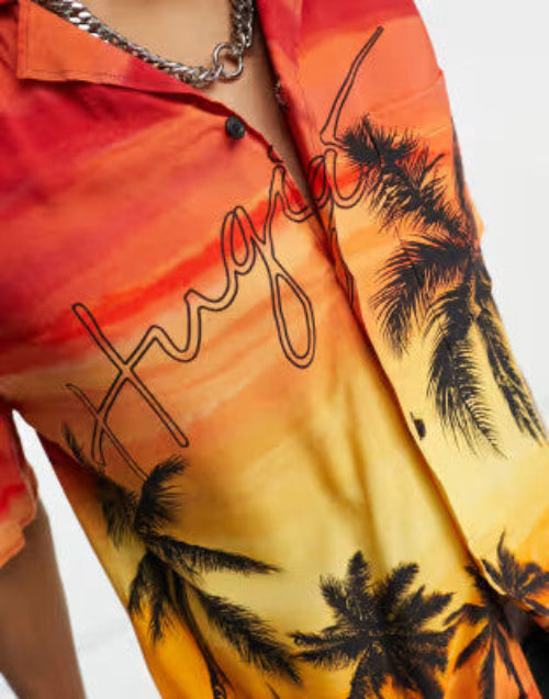 Translation missing: en.Close-up of a short-sleeve button-up shirt with a sunset gradient in orange, yellow, and red, featuring black palm tree silhouettes and a black script graphic across the front